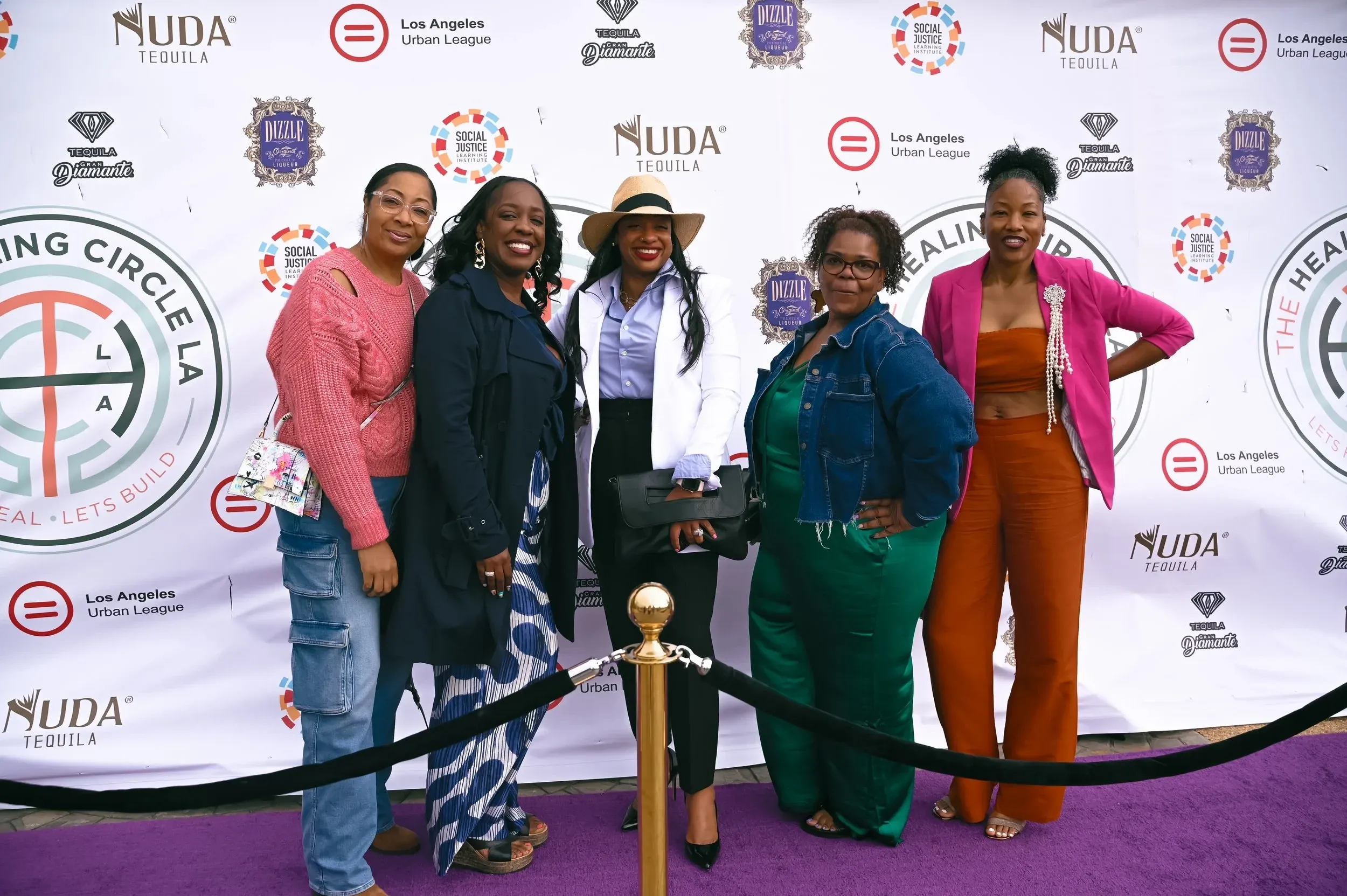 Five Black women smiling on the purple carpet at The Healing Circle LA Black Women's Appreciation Brunch in Los Angeles